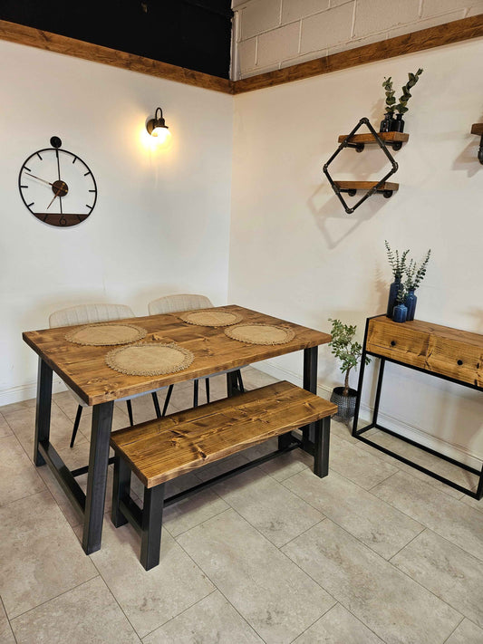 Wooden dining table with benches in a room with a clock and shelves on the wall.